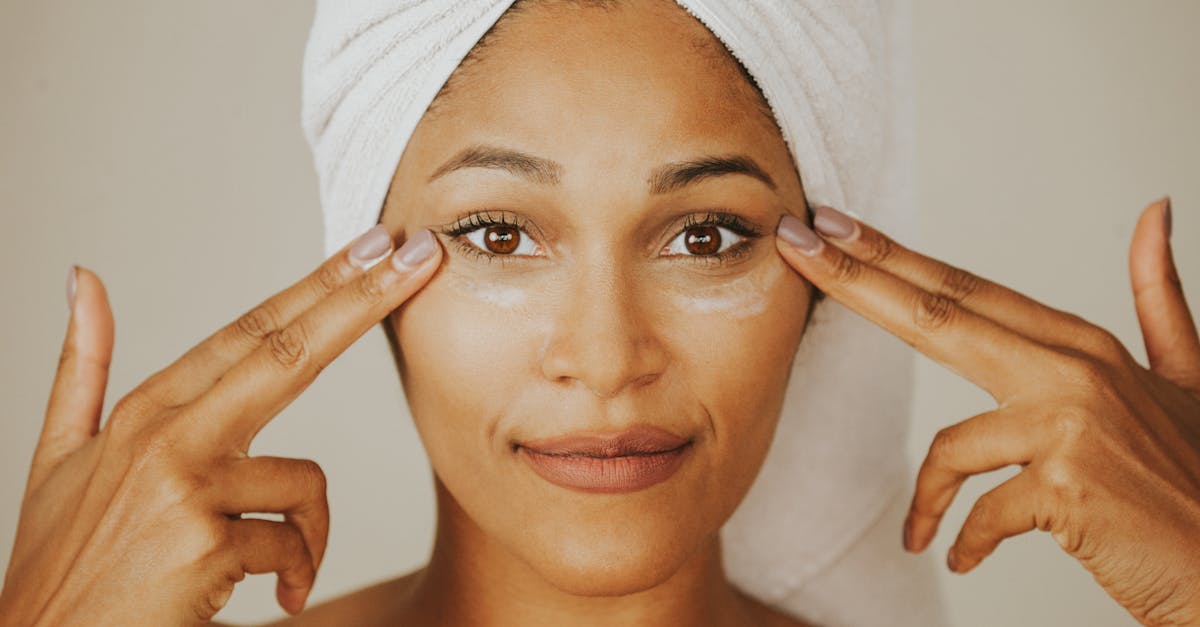 Woman applying facial cream with a towel wrapped on her head, highlighting skincare routine.